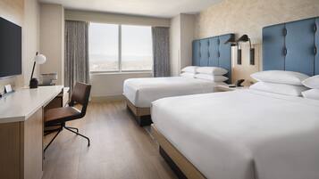 Habitación de hotel con dos camas, un escritorio, una silla y un ventanal con cortinas.