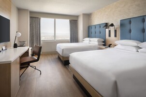 Habitación de hotel con dos camas, un escritorio, una silla y un ventanal con cortinas.