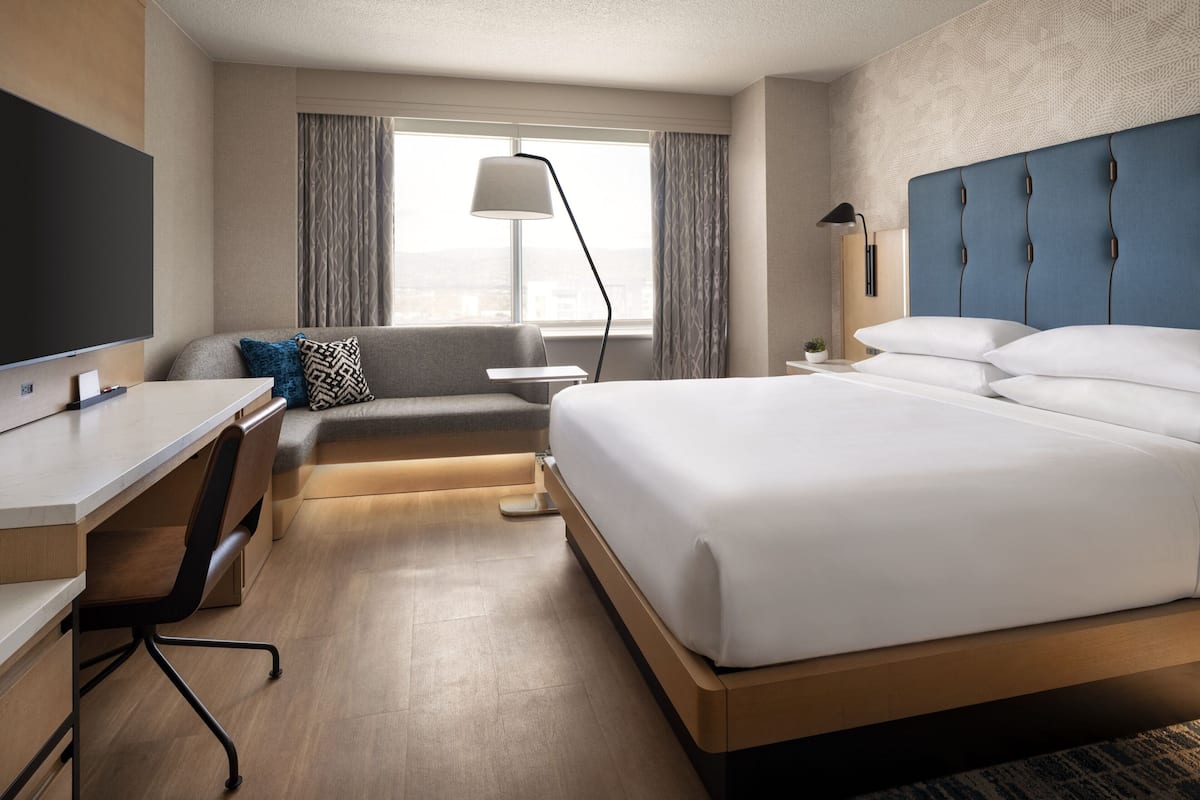 A modern hotel room with a large bed, a desk, a chair, a TV, and a window with curtains.