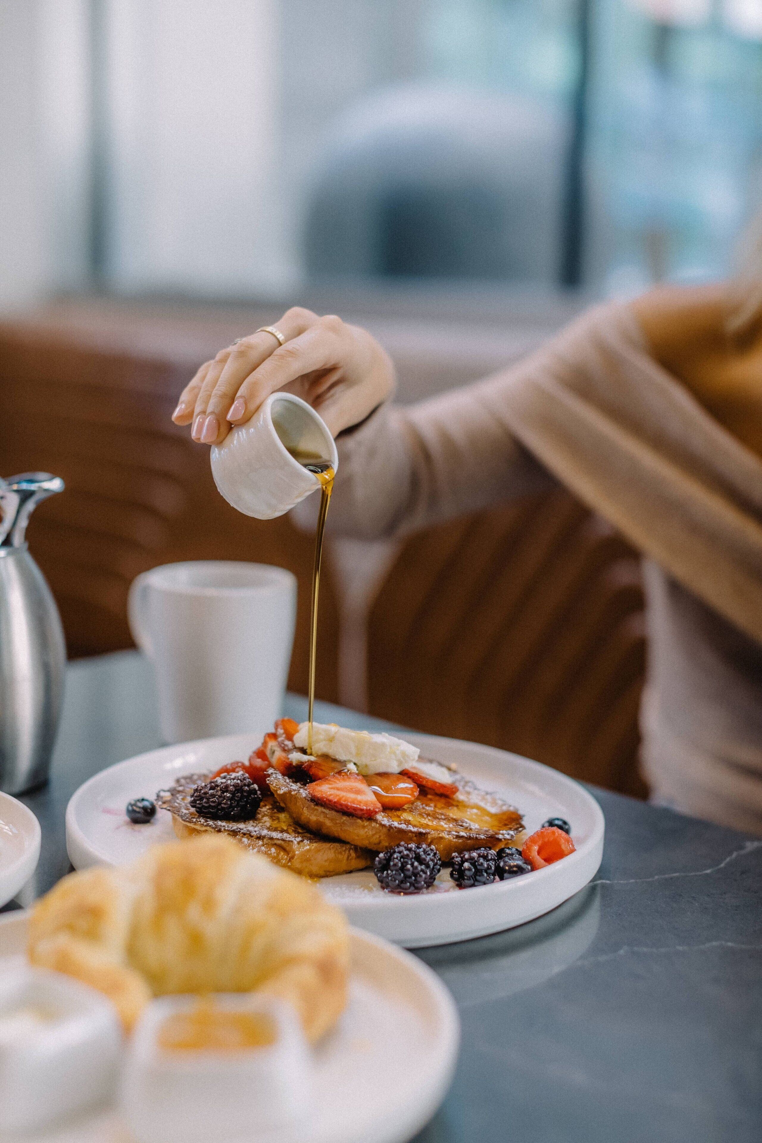 A breakfast setting with a plate of pancakes topped with berries and syrup, a croissant, and a coffee cup.