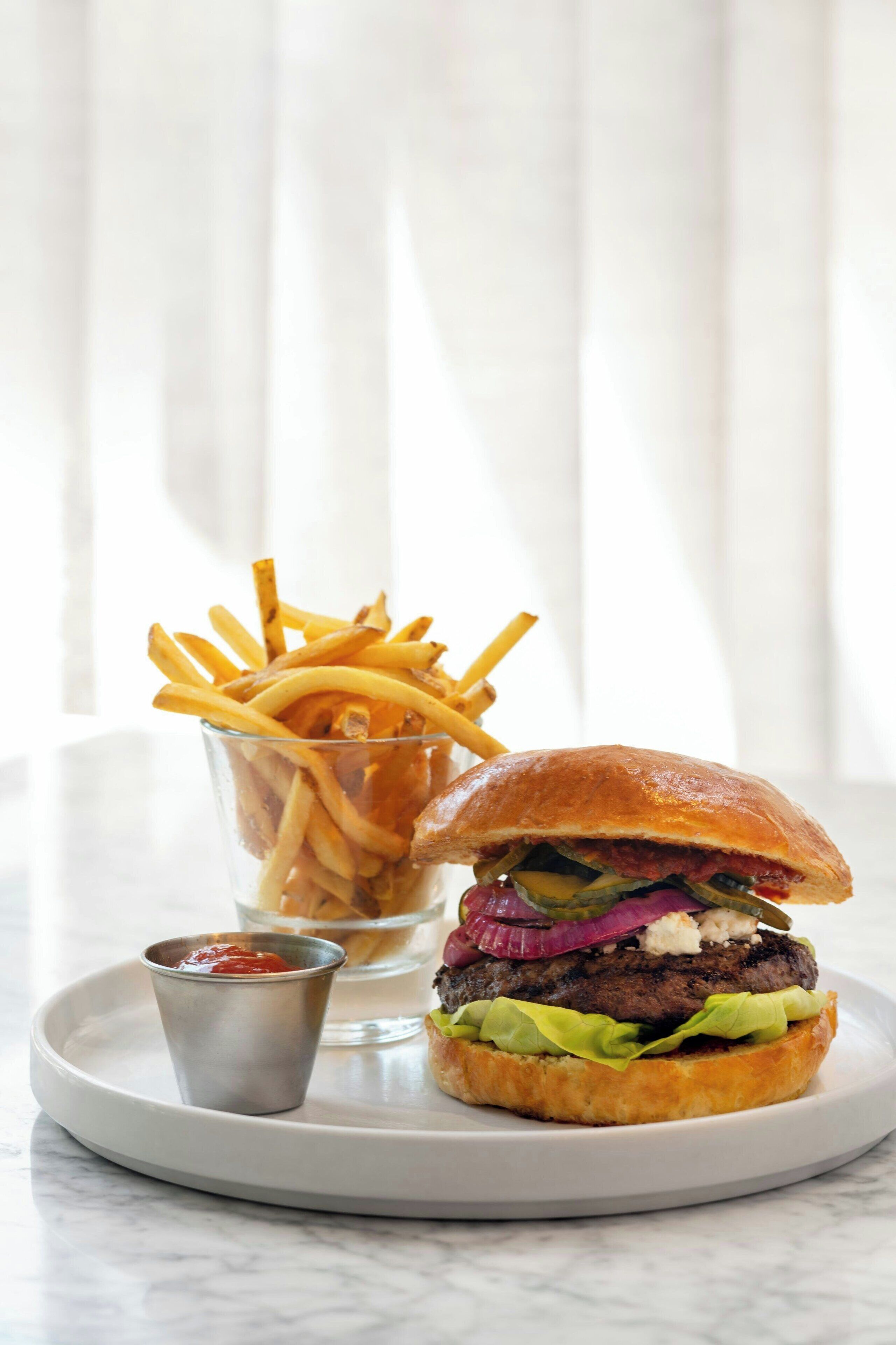 A burger with fries and ketchup on a white plate.