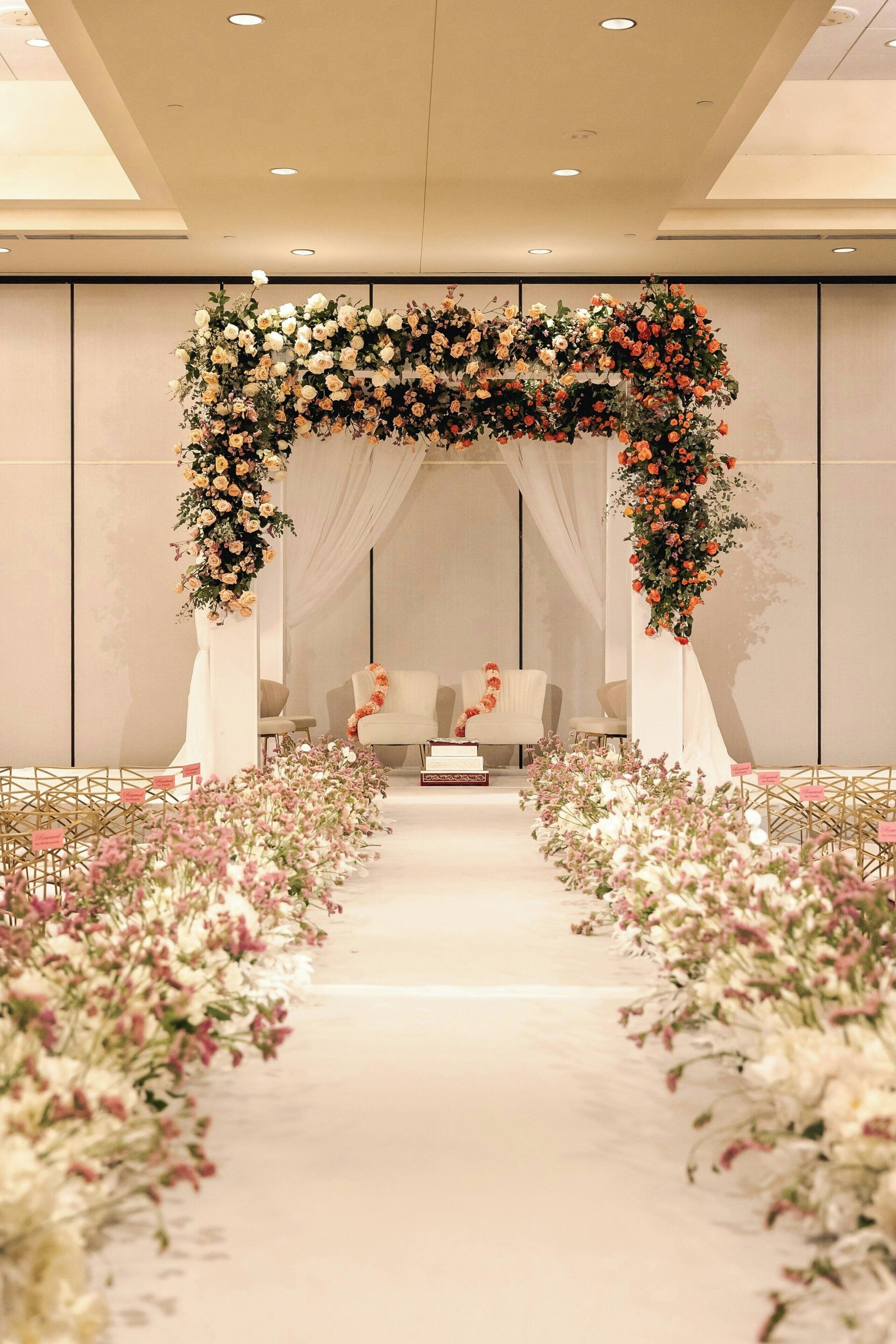 Un pasillo que conduce a un espacio de asientos con un arco floral, sillas y una mesa con una decoración floral.