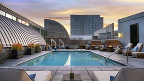 A rooftop pool with lounge chairs and a fire pit, surrounded by modern buildings and a sunset sky. - San Jose Marriott (San Jose)