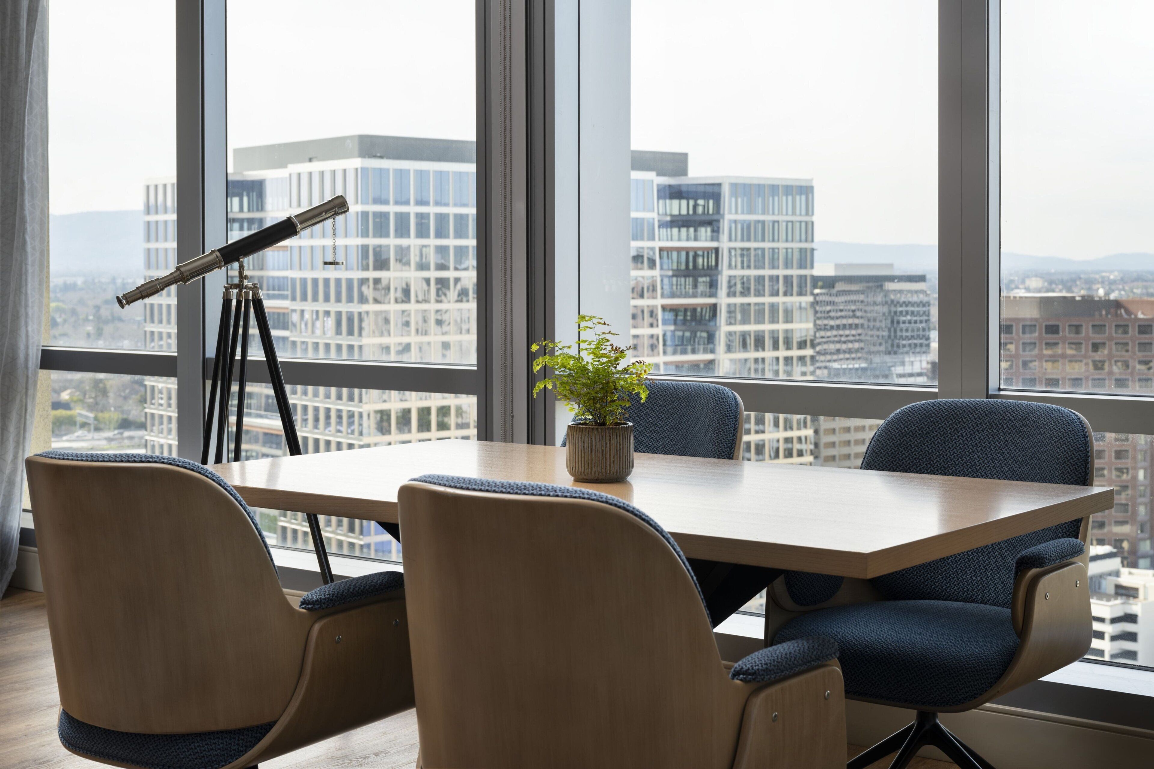 A conference room with a large table, four chairs, a telescope, and a potted plant.