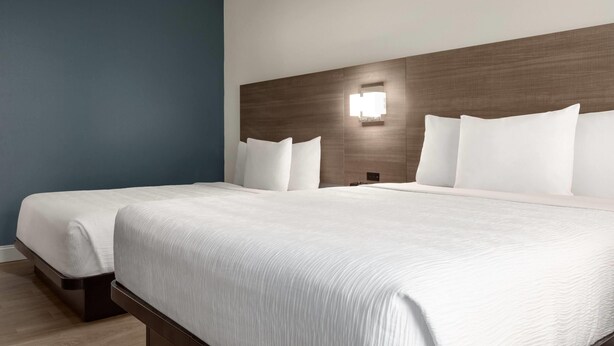 Habitación de hotel con dos camas, pared de acento azul, cabecera de madera y lámpara fijada a la pared.