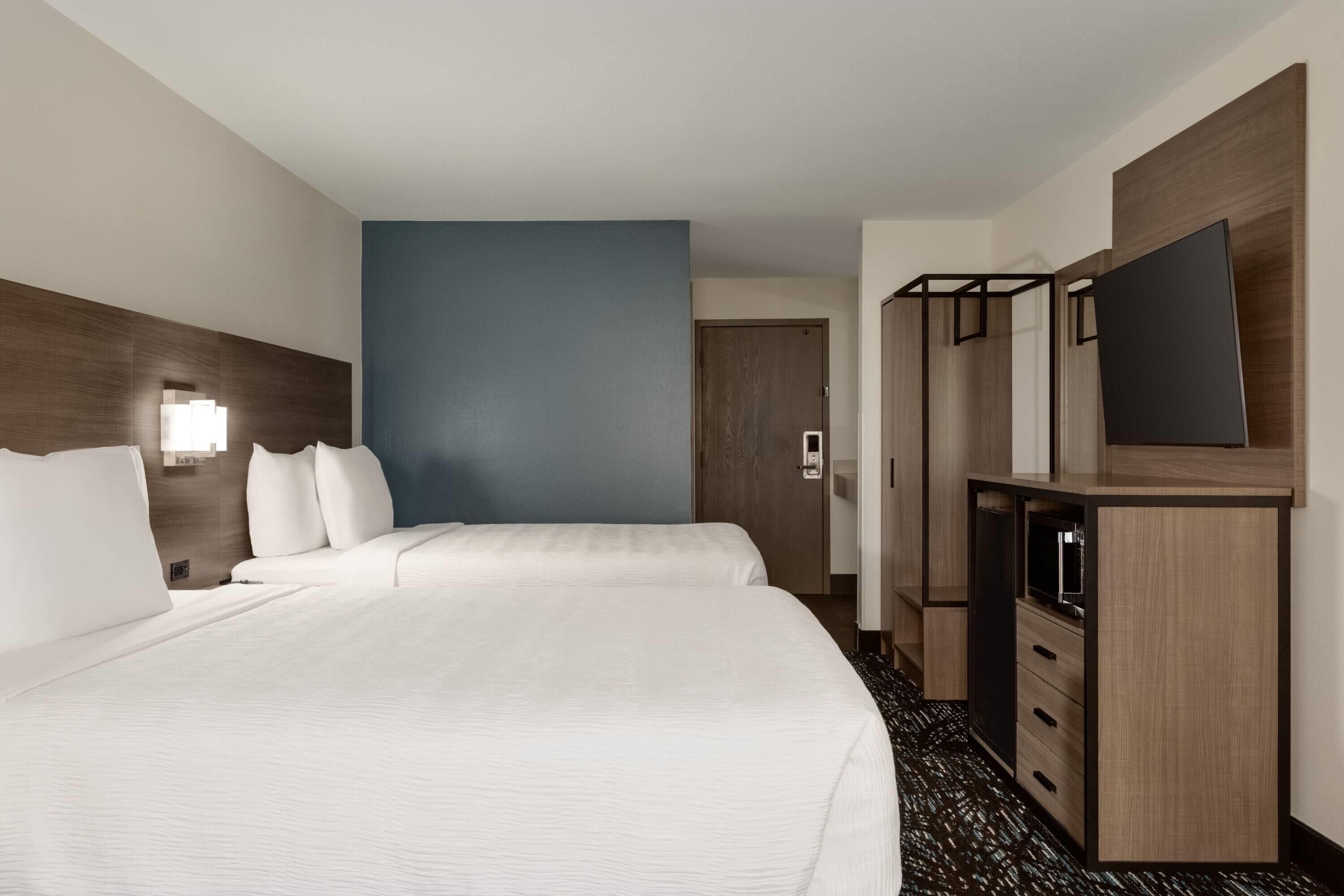 Een hotelkamer met een groot bed, een televisie, een kledingkast en een deur naar een andere kamer.
