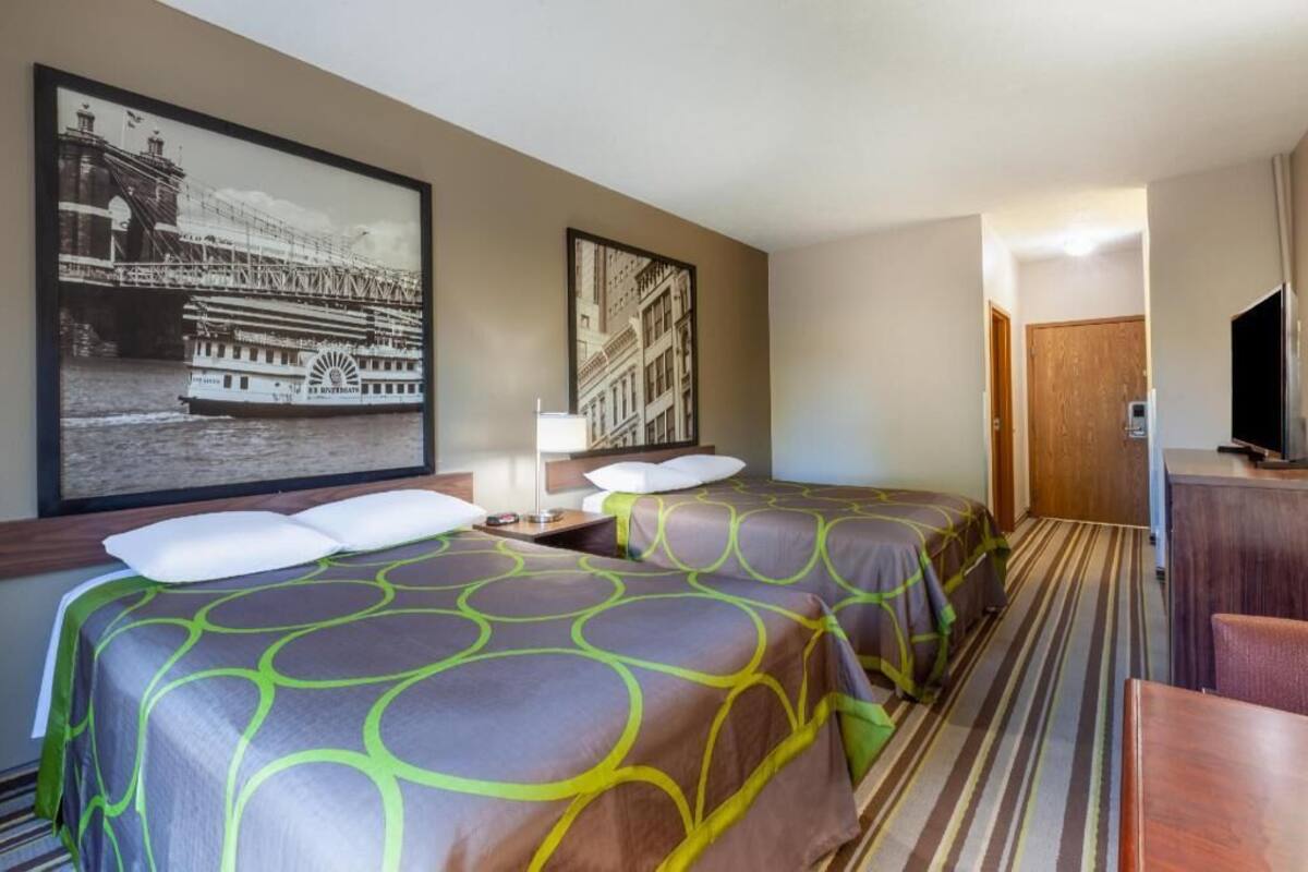 A hotel room with two beds, a desk, a chair, and a television.