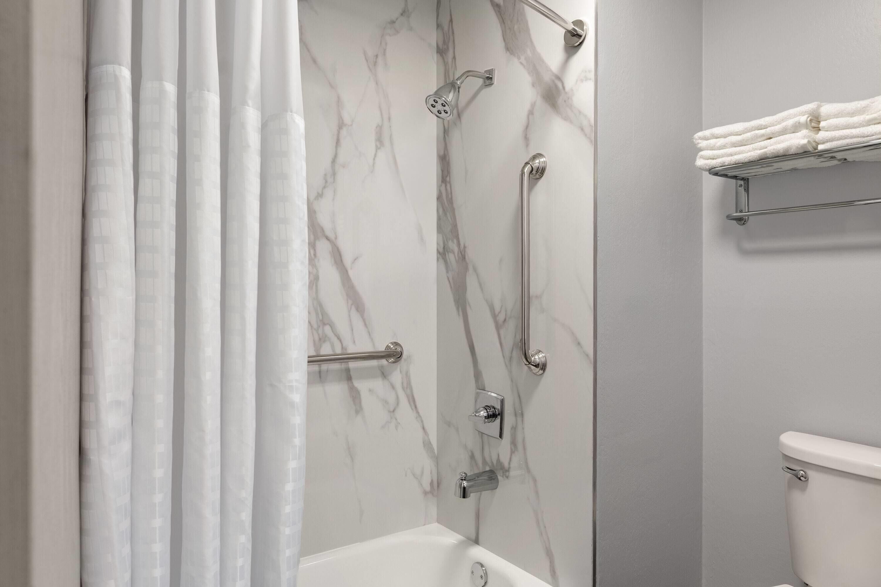 Un baño con bañera, ducha con puerta de vidrio y un perchero para toallas.