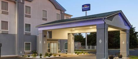 A hotel with a covered entrance, a sign indicating it's a Wyndham property, and a parking lot with marked spaces.