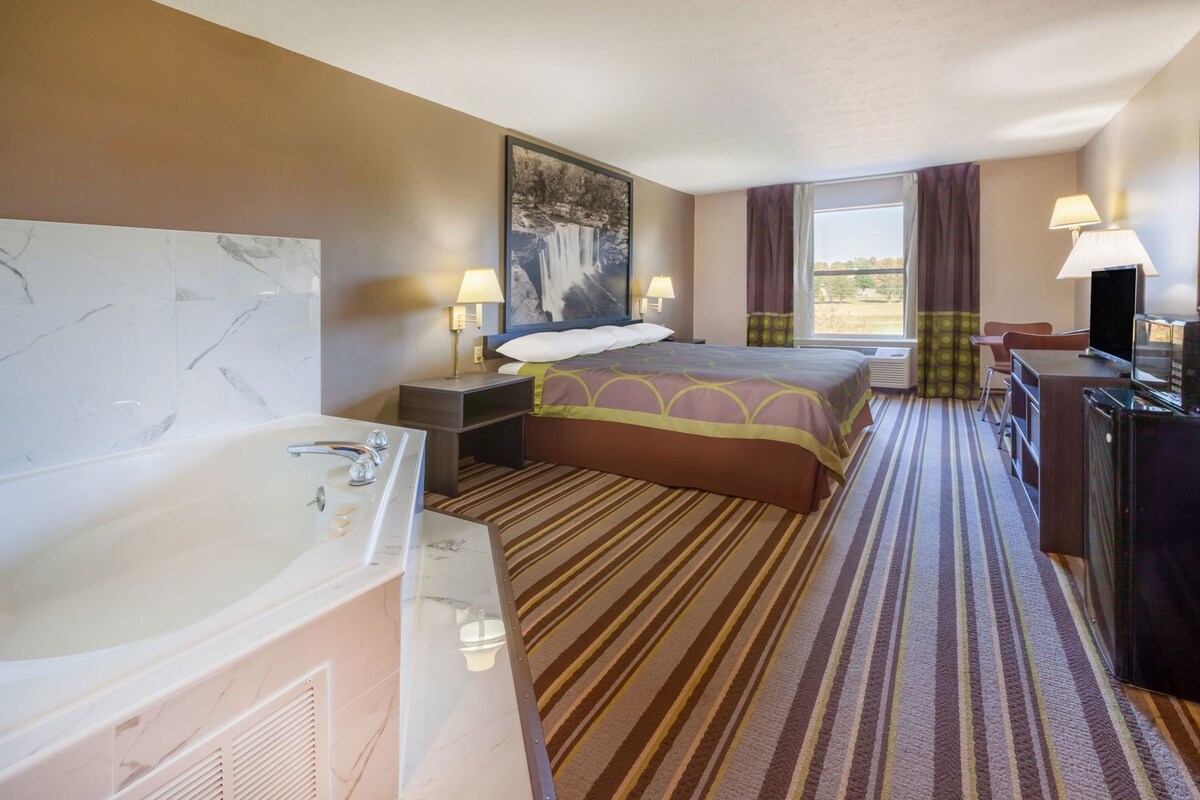 Une chambre d’hôtel avec un grand lit, une salle de bain séparée avec une baignoire, un bureau avec une télévision et une fenêtre avec des rideaux.