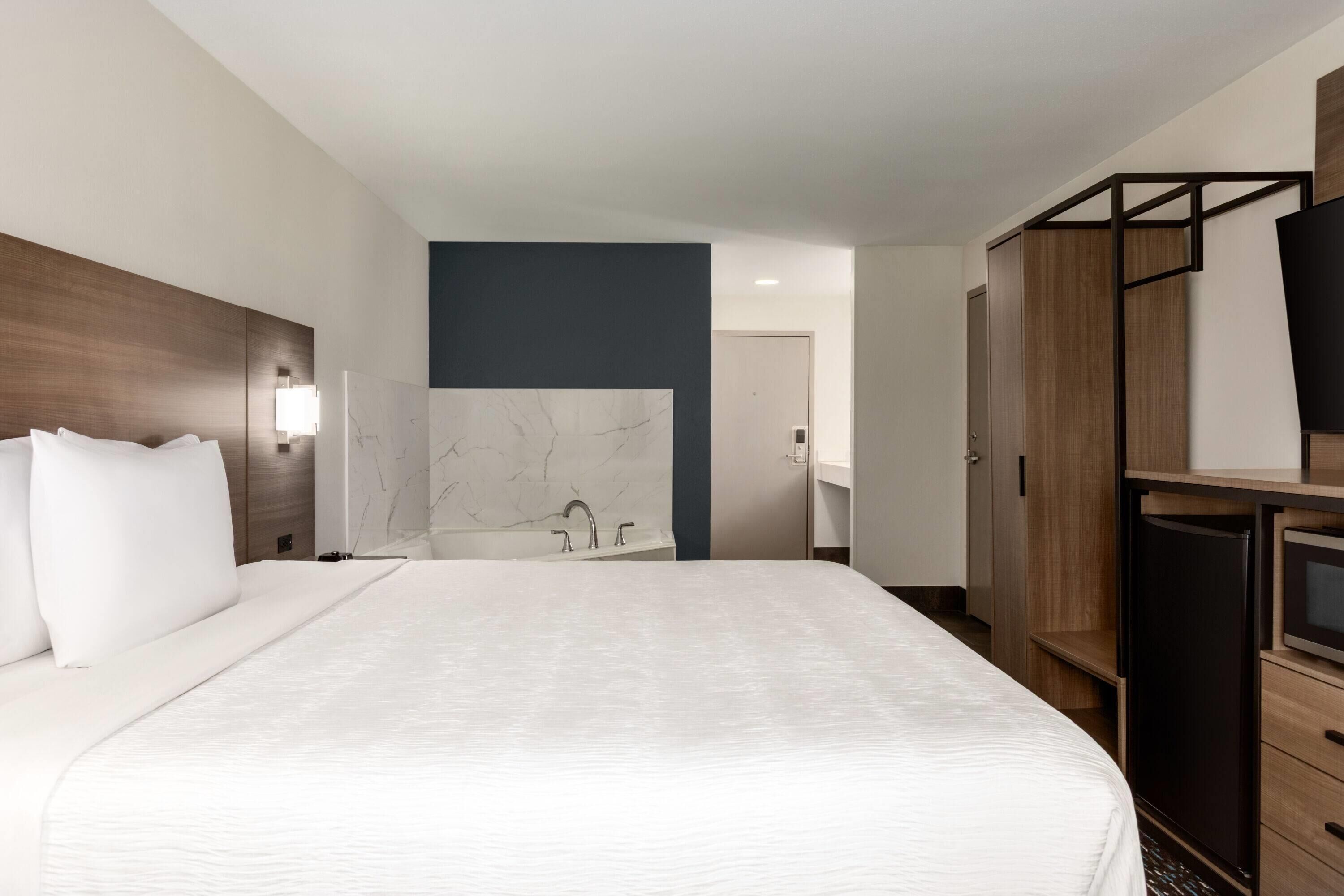 Une chambre d’hôtel avec un grand lit, une armoire en bois, une télévision et un mur en marbre.
