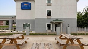 Un hotel con un letrero que dice 'Baymont by Wyndham' y un acceso cubierto. Hay mesas de picnic al frente.