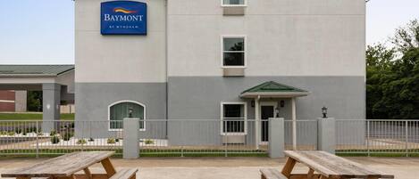 Un hôtel avec une enseigne indiquant « Baymont by Wyndham » et une entrée abritée. On y trouve des tables de pique-nique à l’avant.