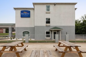 Un hotel con un letrero que dice 'Baymont by Wyndham' y un acceso cubierto. Hay mesas de picnic al frente.