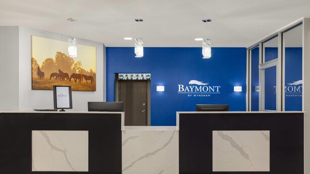 Un área de recepción con pared azul, un cuadro con caballos y el logotipo de Baymont.