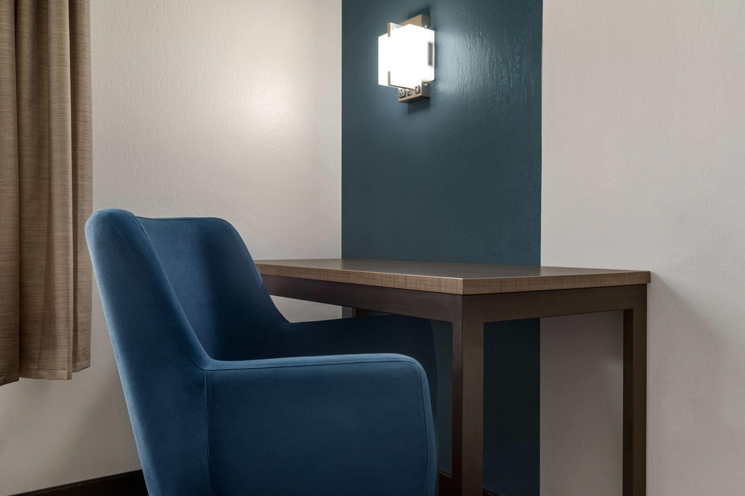 A room with a single blue chair, a small table, and a wall-mounted light fixture.