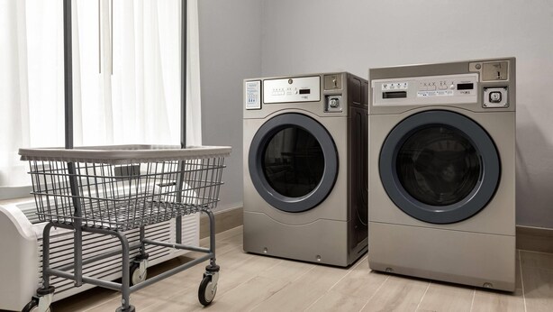 A laundry area with two front-loading washing machines, a metal cart, and a window with blinds.