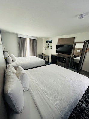 Ein Hotelzimmer mit zwei Betten, einem Fernseher, einem Schreibtisch und einem Spiegel.