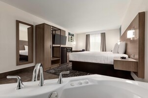 Habitación de hotel con una bañera grande, una cama, un escritorio y un televisor.