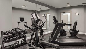 Un gimnasio con equipo de ejercicio, una cinta de correr y un espejo que refleja la sala.
