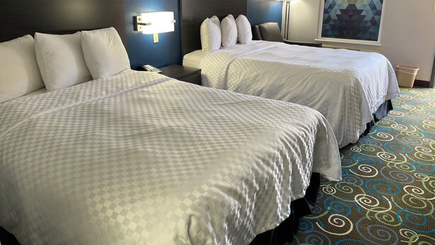A hotel room with two beds, a blue wall, and a geometric-patterned window. - Clairmont Inn & Suites Warren (Warren)