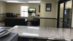 A hotel lobby with a seating area, a television, a printer, and a reception desk. - Clairmont Inn & Suites Warren (Warren)