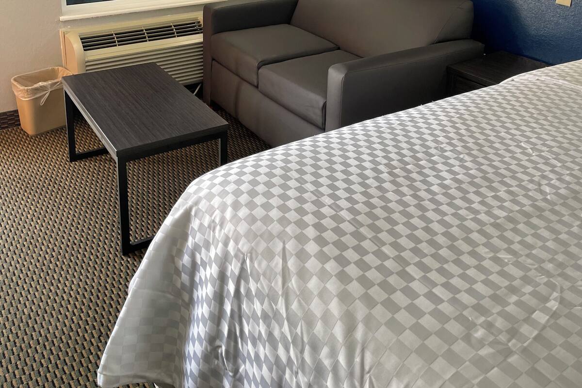Hotellihuone, jossa on sänky, sohva, pieni pöytä, lattiavalaisin ja ikkuna, jossa on geometrinen kuvio.
