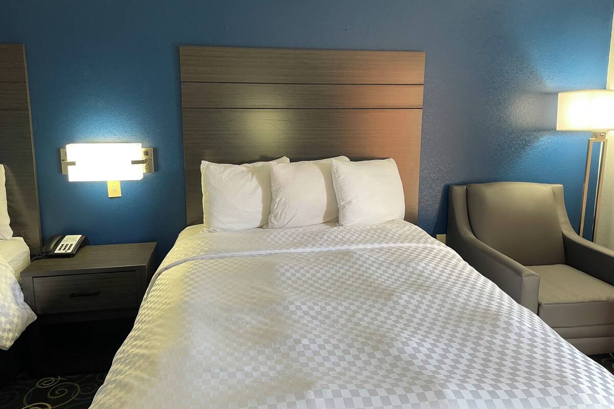 Hotellihuone, jossa on suuri sänky, yöpöytä, jossa on puhelin, tuoli ja seinään kiinnitetty valaisin.