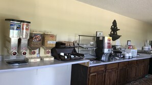 A self-service breakfast bar with various food and beverage dispensers, including frosted flakes, corn flakes, and a Folgers coffee machine. - Clairmont Inn & Suites Warren (Warren)