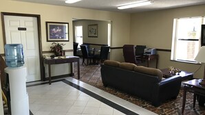 A hotel lobby with a reception desk, a water cooler, a sofa, and a dining area with chairs and tables. - Clairmont Inn & Suites Warren (Warren)