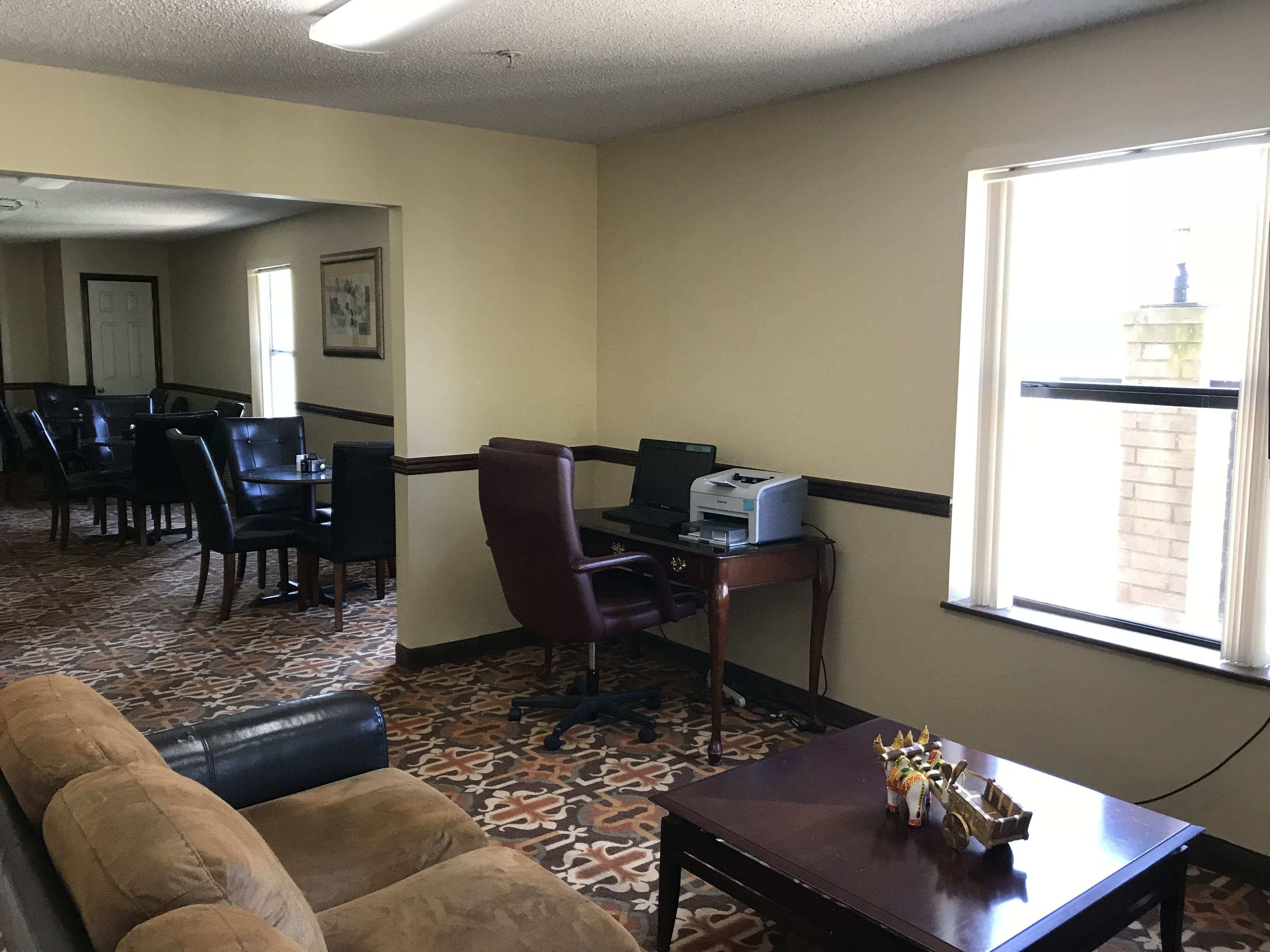 Ein Hotelzimmer mit Essbereich, einem Schreibtisch inklusive Drucker, einer Couch und einem kleinen Tisch mit Dekoration.