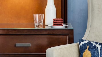 A wooden dresser with a white vase, a glass, and a plate of cookies.