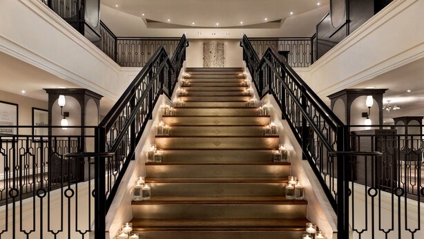 A grand staircase with multiple steps, black railings, and lit candles on each step.