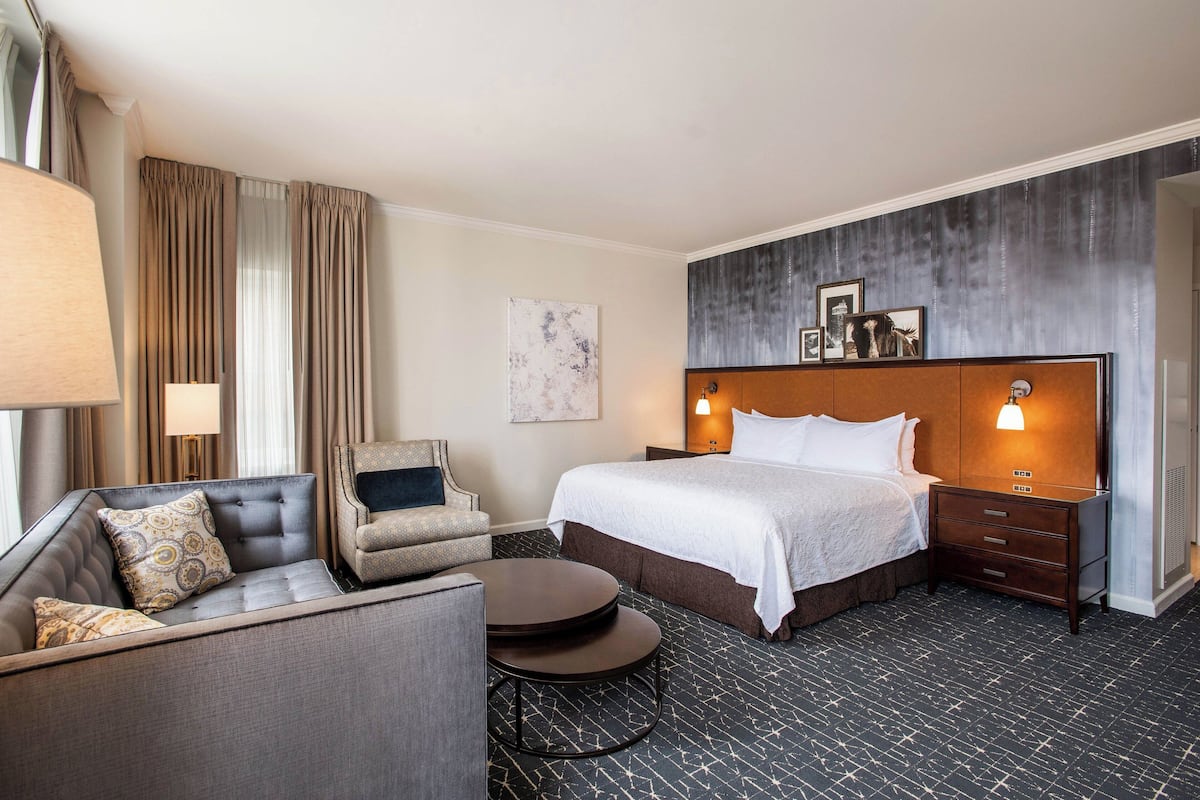 Ein Hotelzimmer mit einem Bett, einer Couch, einem Sessel, einem kleinen Tisch und einer Wandlampe.