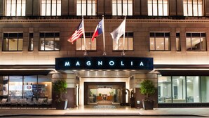 The exterior of the Magnolia hotel with three flags, a large entrance, and a modern facade.