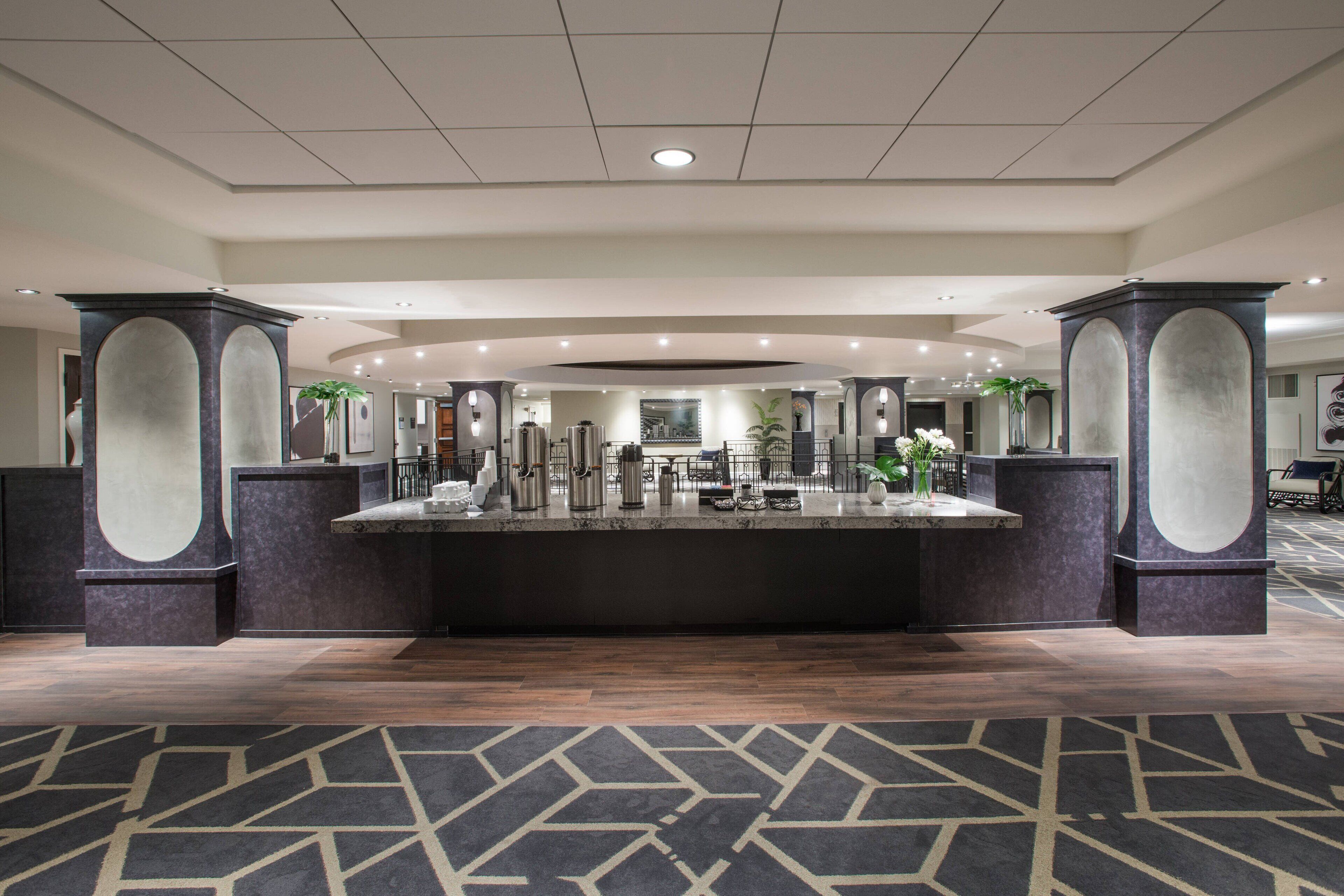 A hotel lobby with a central reception desk, large pillars, and a patterned carpet.