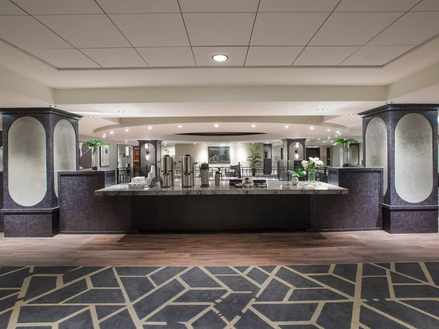 A hotel lobby with a central reception desk, large pillars, and a patterned carpet.