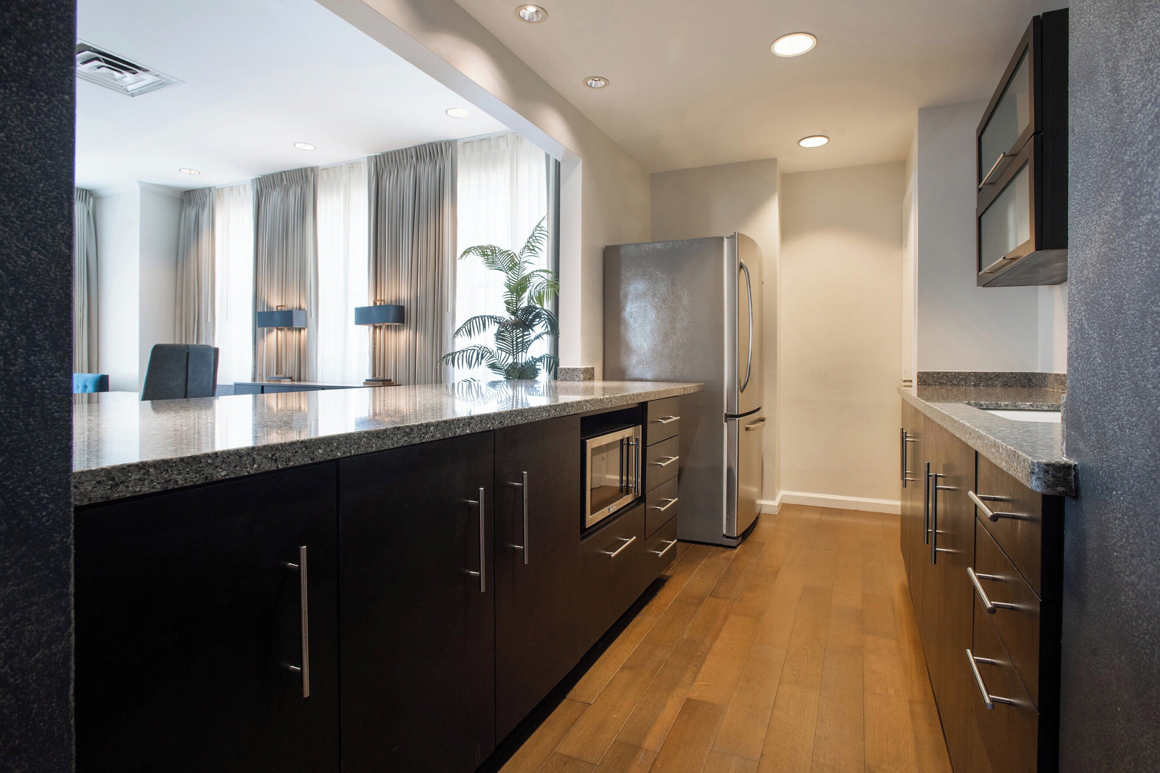 A modern kitchen with dark cabinetry, a stainless steel refrigerator, and a granite countertop.