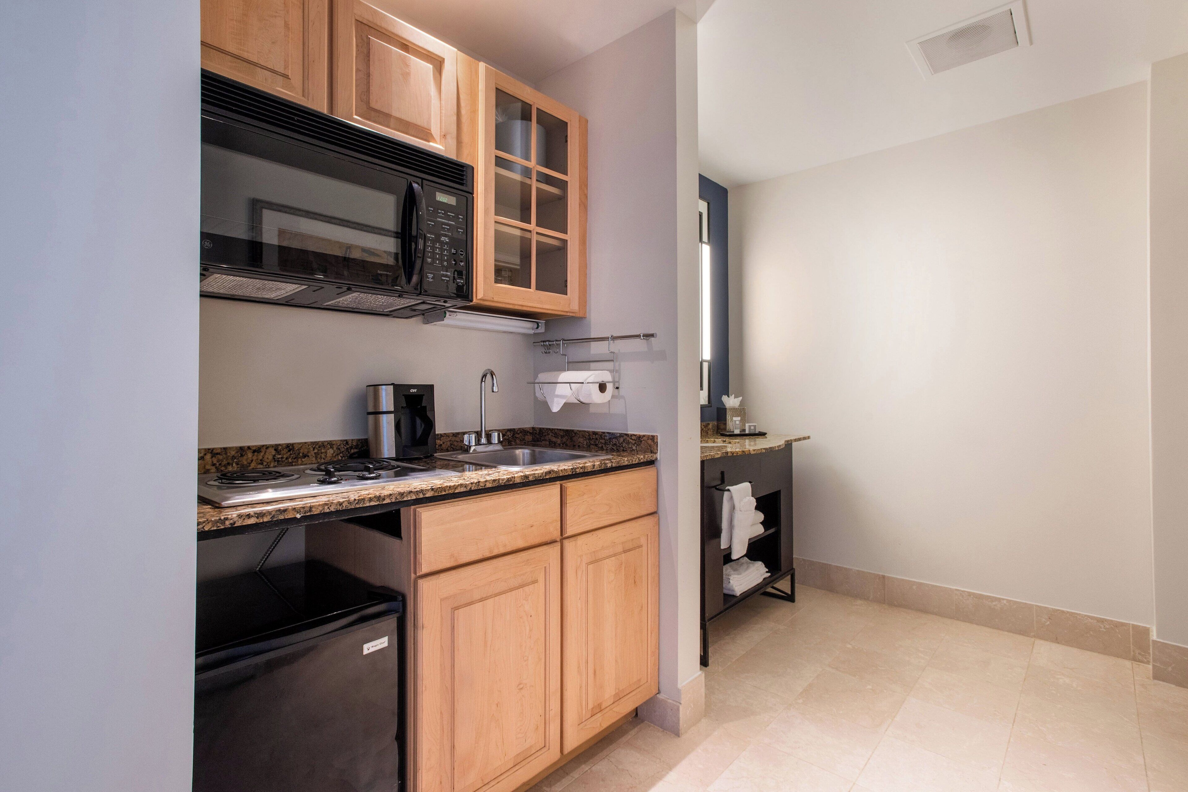 A compact kitchen with wooden cabinets, a stainless steel sink, a microwave, and a coffee maker.