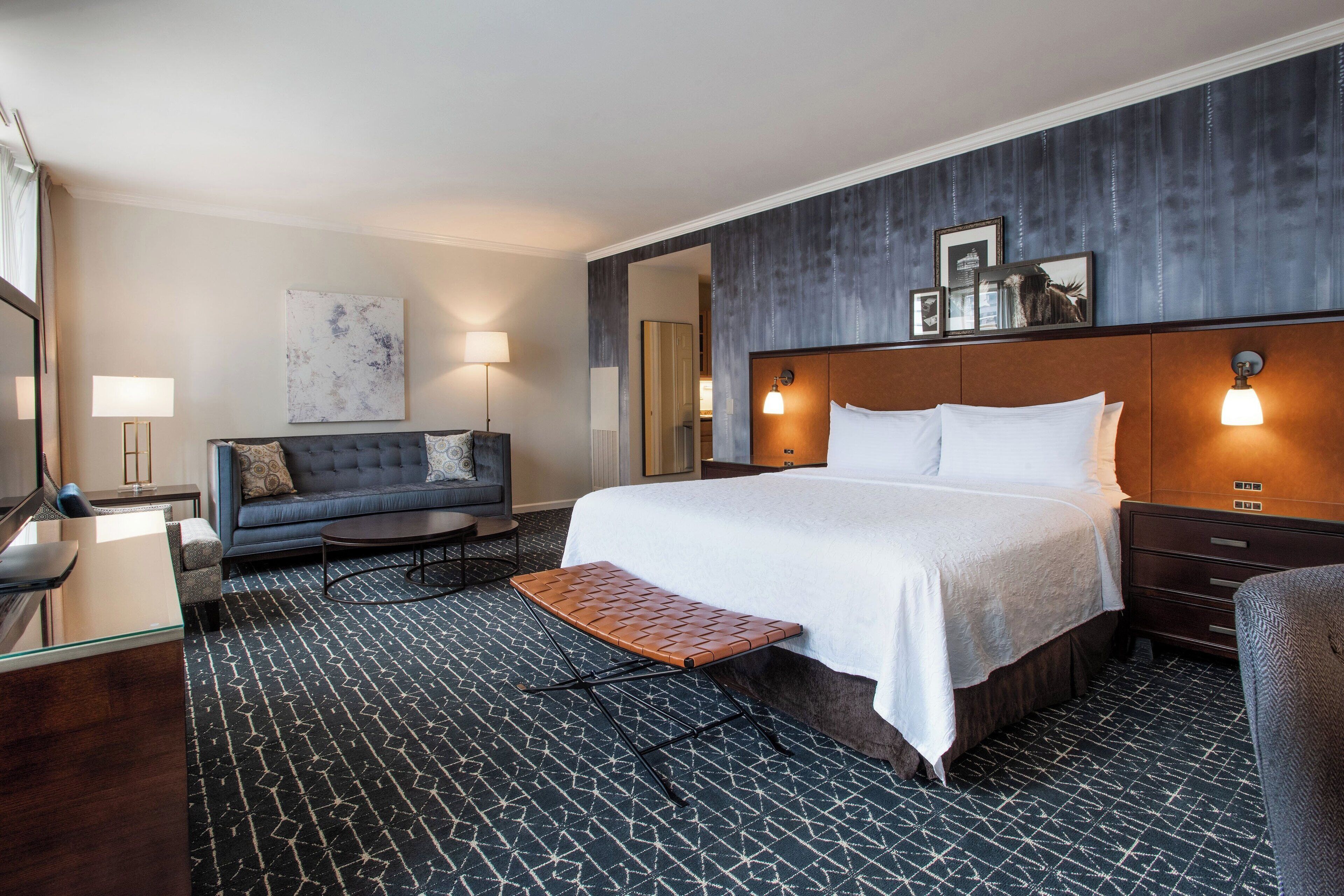 A hotel room with a large bed, a sofa, a desk, and a mirror.