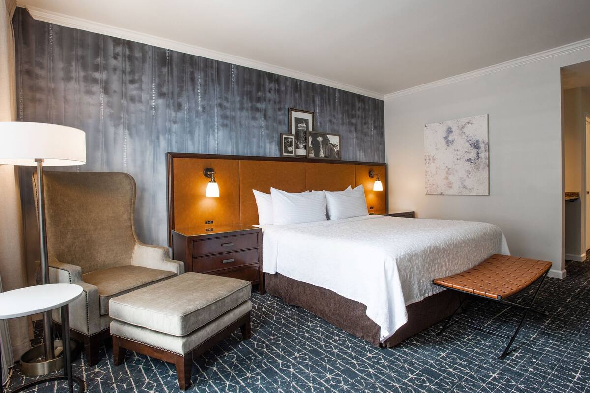 Ein Hotelzimmer mit einem großen Bett, einem Sessel, einem kleinen Tisch und einer Bank.