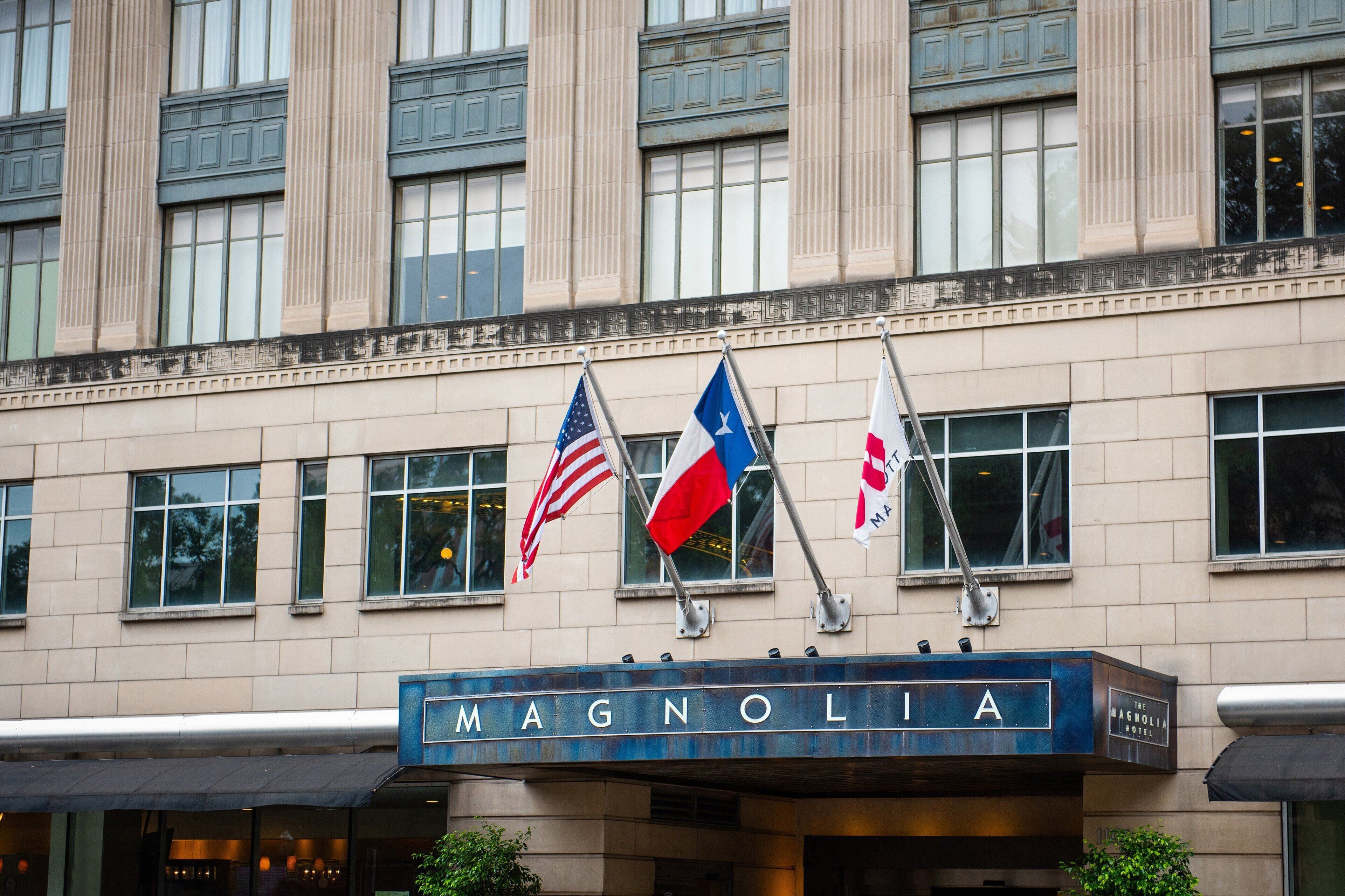 The exterior of the Magnolia Hotel with flags, including the American flag, and a sign with the hotel's name.