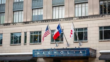 The exterior of the Magnolia Hotel with flags, including the American flag, and a sign with the hotel's name.