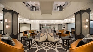 A spacious lobby with a high ceiling, a central seating area with two sofas, and a patterned carpet.