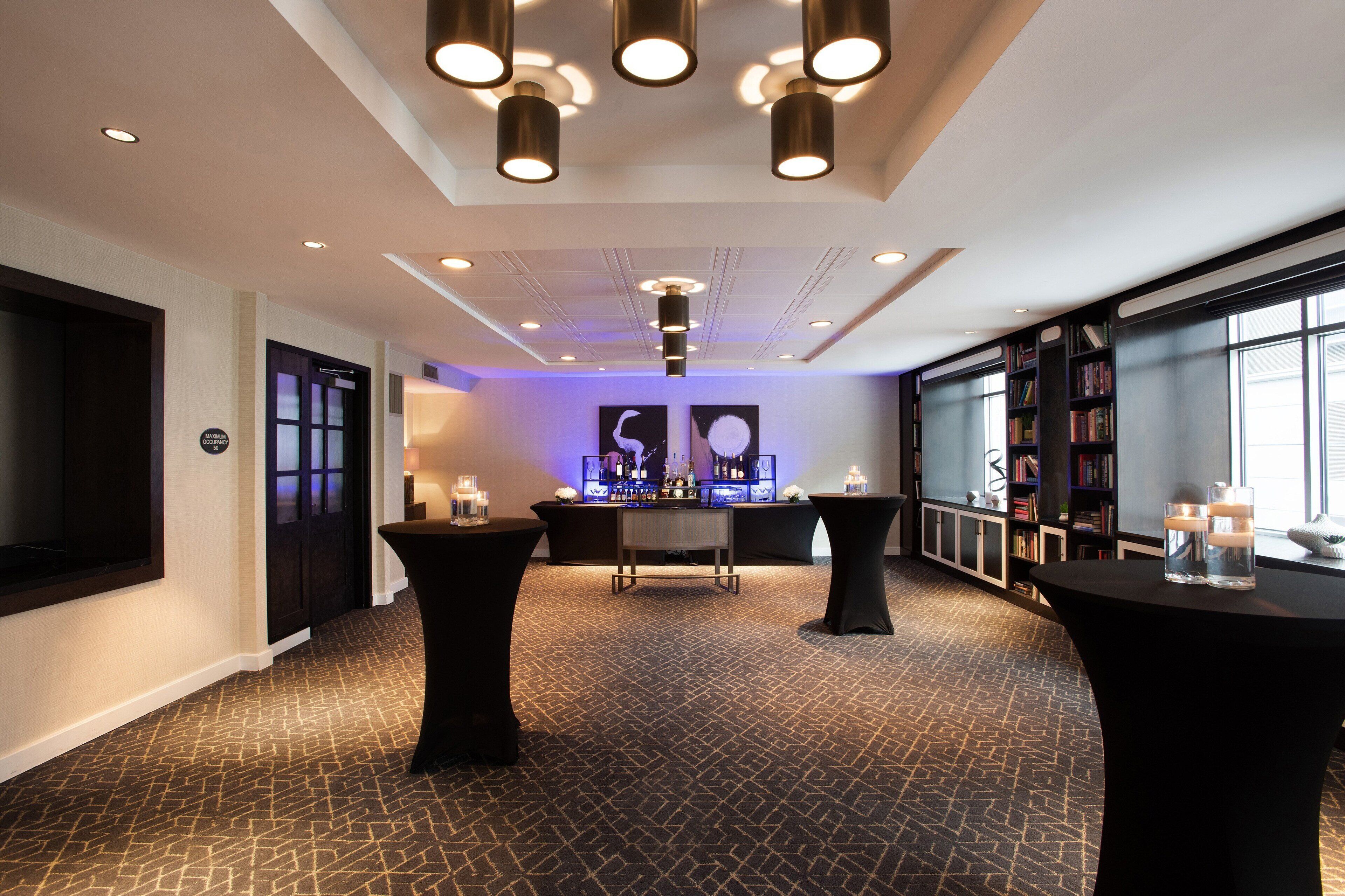 Un hall d’hôtel moderne avec un comptoir d’accueil central, des tables noires et une bibliothèque.