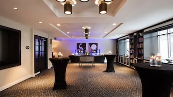 Un lobby moderno de hotel con una recepción central, mesas negras y una estantería.