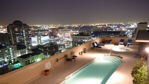 A rooftop pool with lounge chairs and a city view at night.