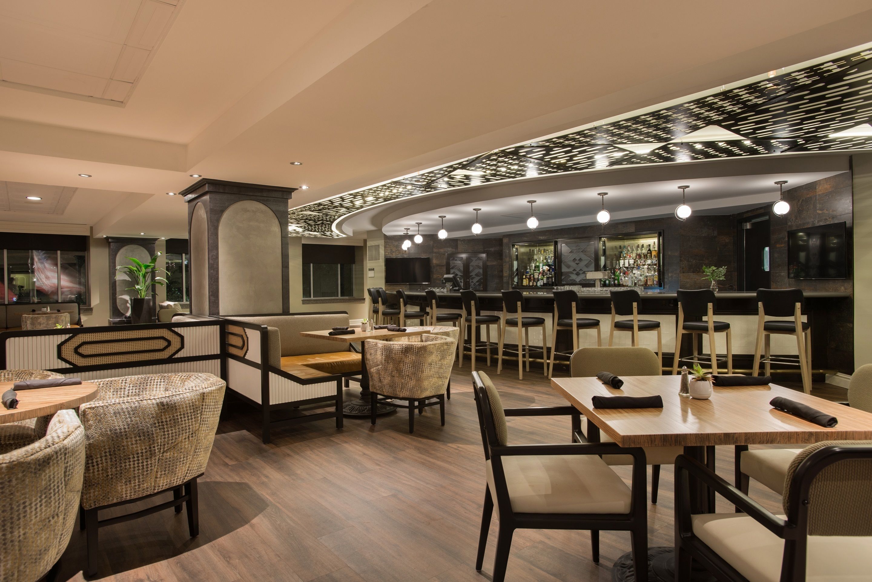 A modern restaurant with a bar area, wooden tables, and wicker chairs.