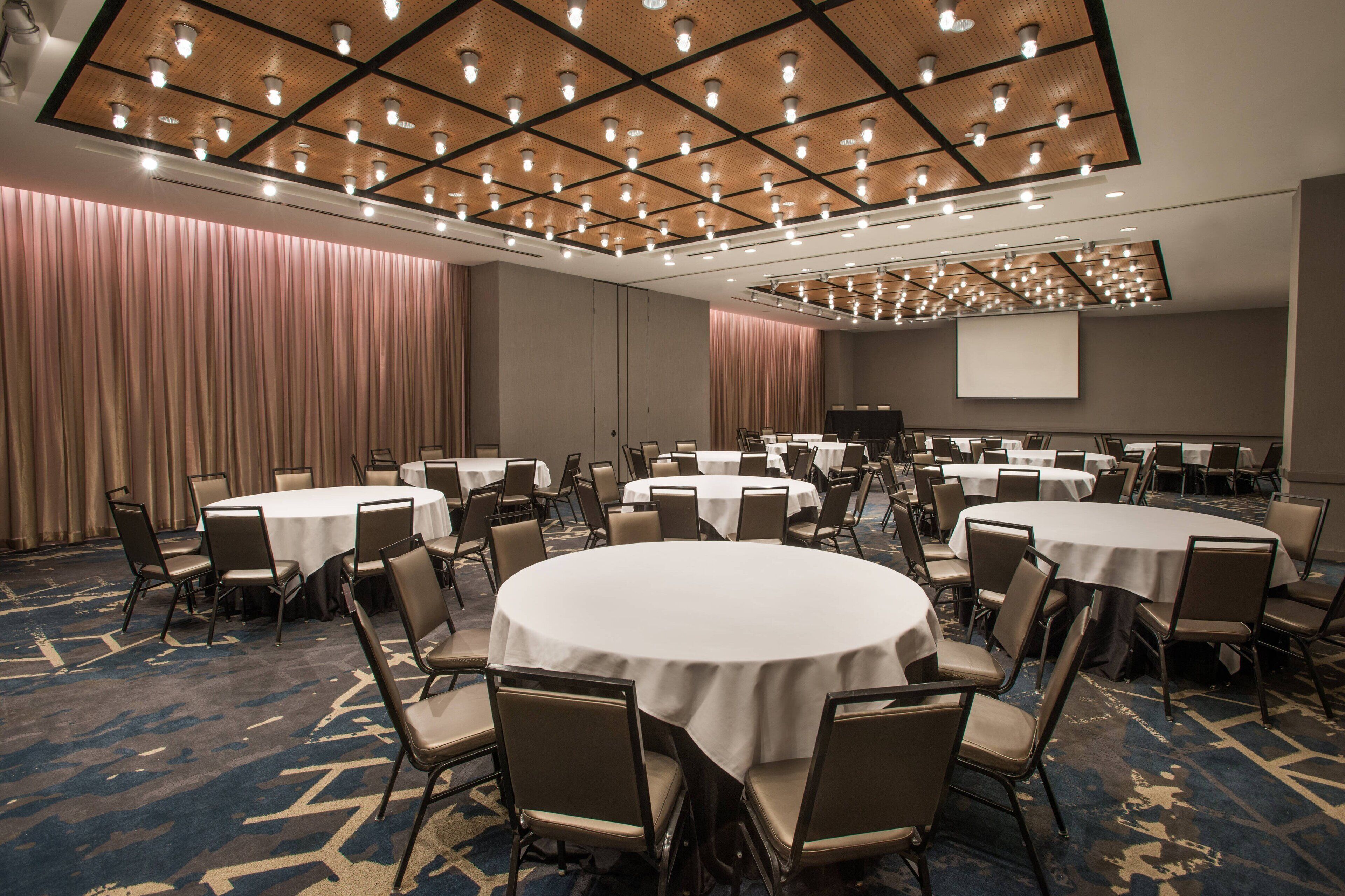 A conference room with multiple round tables, chairs, and a large screen.