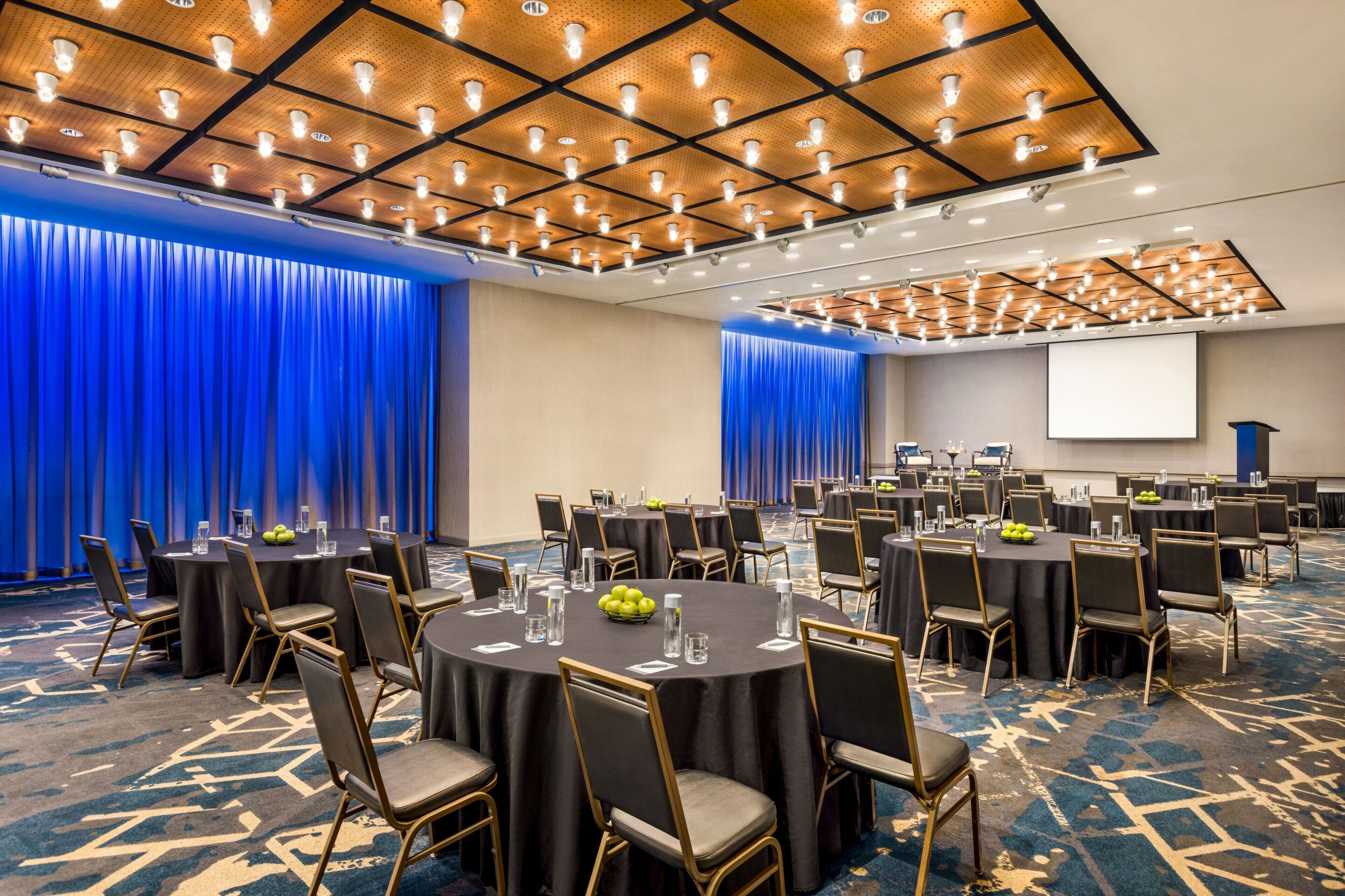 A conference room with round tables, chairs, and a projector screen.